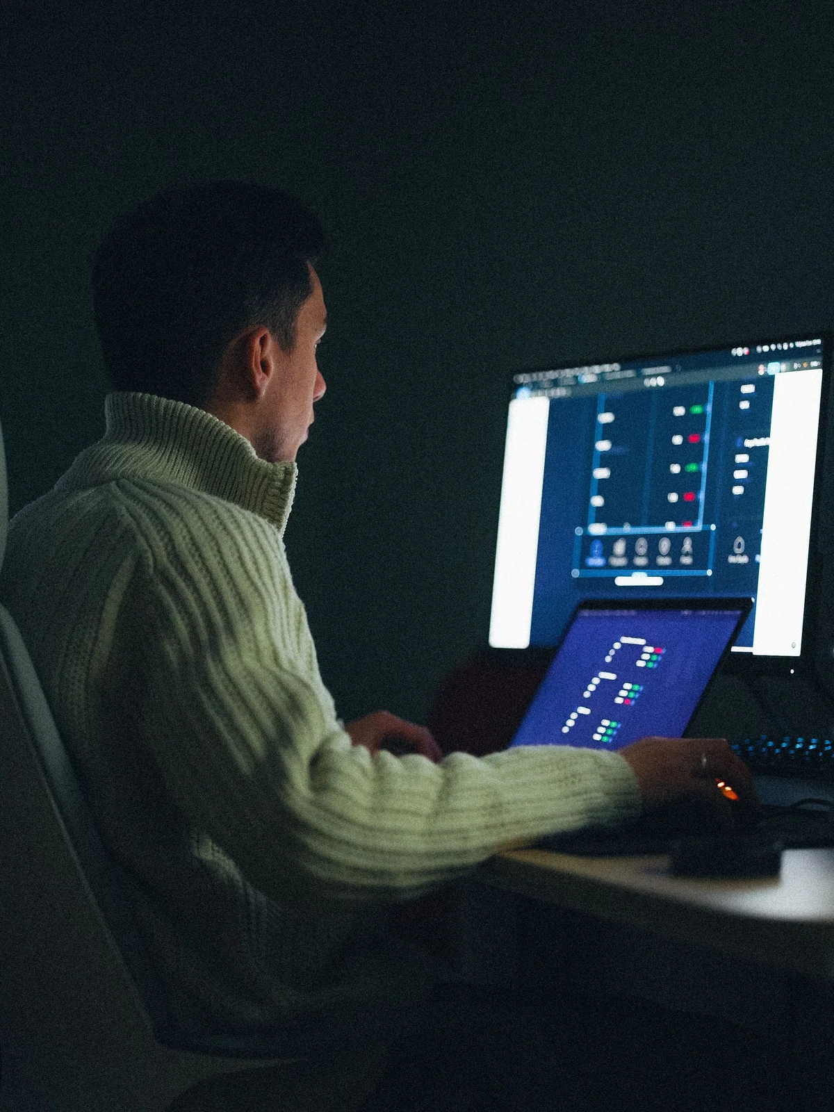 An AI developer coding at dual monitors in a dark studio