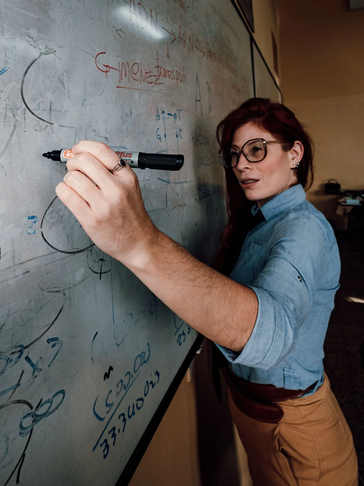An educator writing equations on a glass whiteboard — teaching, not just coding